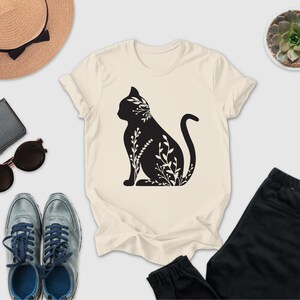a casual outfit consisting of a white t-shirt with a black cat silhouette, a pair of gray sneakers, a pair of black pants, sunglasses, a hat, and a small potted succulent plant.