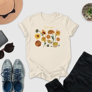 a casual outfit consisting of a white t-shirt with a floral design, a pair of sunglasses, a hat, a wallet, a pair of sneakers, and a pair of pants.