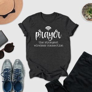 a casual outfit consisting of a black t-shirt with a white text design, a pair of sunglasses, a hat, a wallet, a potted succulent, and a pair of sneakers.