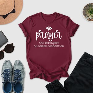 a collection of items, including a maroon t-shirt with the text "prayer the strongest wireless connection", a hat, sunglasses, a wallet, a potted succulent, and a pair of sneakers.
