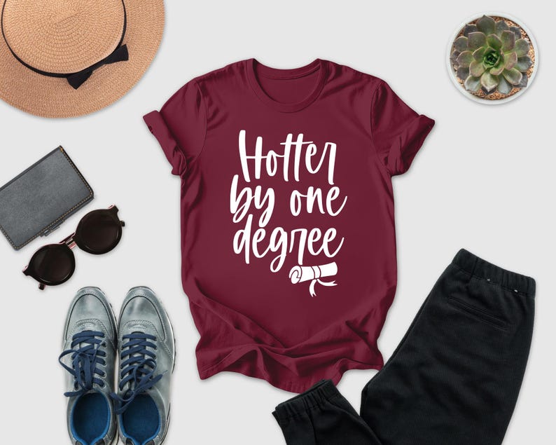 a casual outfit consisting of a burgundy t-shirt with the text "Hotter by one degree", a pair of black pants, a pair of sunglasses, a hat, and a small potted plant.