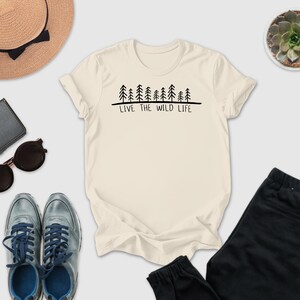 a casual outfit consisting of a white t-shirt with a graphic design, a pair of sunglasses, a hat, a wallet, a pair of sneakers, and a potted succulent plant.