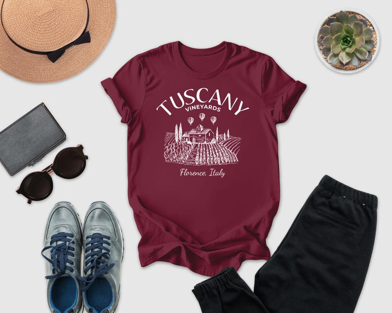 a collection of items, including a burgundy T-shirt with a graphic of a vineyard, sunglasses, a hat, a wallet, a pair of shoes, and a potted succulent.