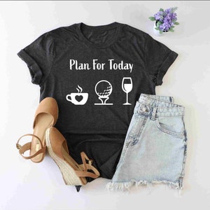 Peut inclure: Un t-shirt gris fonc&eacute; avec le texte "Plan for Today" et des ic&ocirc;nes blanches d'une tasse de caf&eacute;, d'une balle de golf sur un tee et d'un verre &agrave; vin.