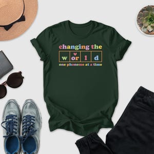 a green t-shirt with a colorful graphic design, along with various clothing items and accessories such as sunglasses, a hat, and a potted plant.