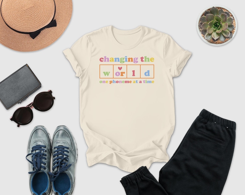 a casual outfit consisting of a white t-shirt with a colorful graphic, sunglasses, a hat, a wallet, a potted plant, and a pair of shoes.