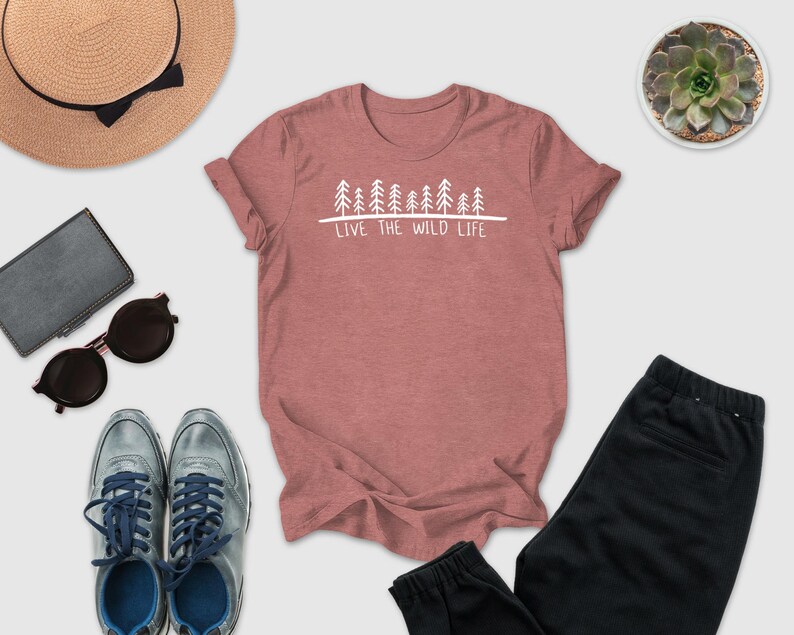 A pink t-shirt with the text "LIVE THE WILD LIFE" printed on it, along with a pair of sunglasses, a hat, a wallet, a potted succulent, and a pair of sneakers.