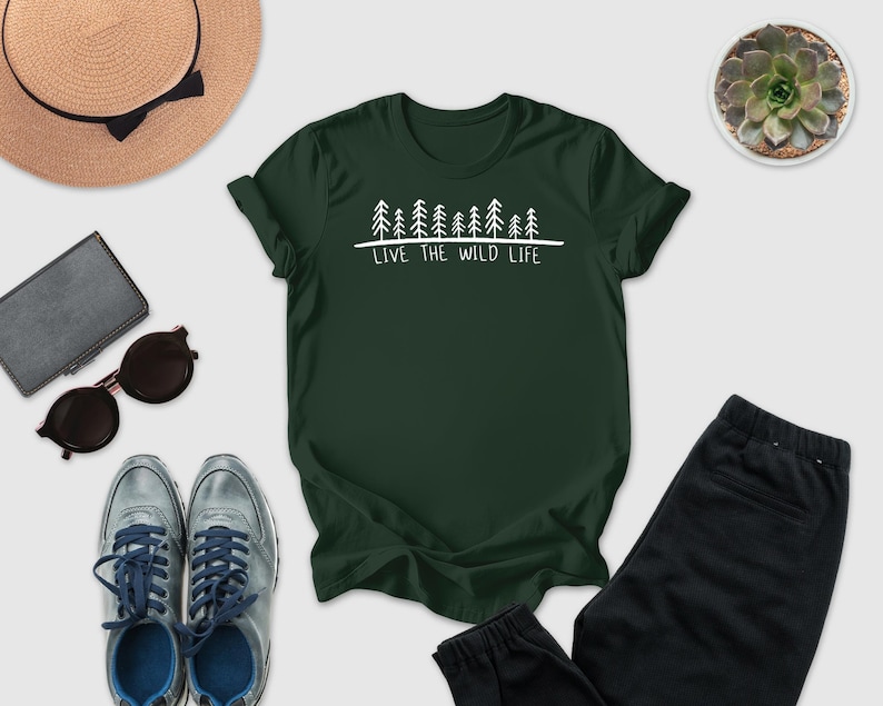 a collection of outdoor-themed items, including a green t-shirt with a tree graphic and the text "Live the wild life", a hat, sunglasses, a wallet, a potted succulent, and a pair of sneakers.