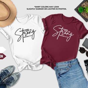 a pair of white and maroon t-shirts with the text "She is Strong" printed on them, along with a pair of jeans, sunglasses, a hat, and a wallet. The text "SHIRT COLORS MAY LOOK SLICTER OR Lighter IN PHOTOS" is also present, suggesting that the colors of the shirts may appear slightly different in photos.
