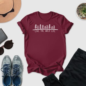 A maroon t-shirt with the text "LIVE THE WILD LIFE" printed on it, along with a pair of sunglasses, a hat, a wallet, a potted succulent, and a pair of sneakers.