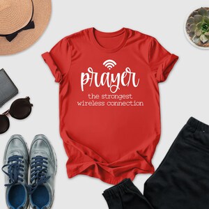a red t-shirt with the text " Prayer the strongest wireless connection" printed on it, along with a pair of sunglasses, a hat, a wallet, and a potted succulent plant.