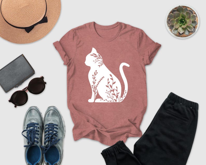 a casual outfit consisting of a pink t-shirt with a white cat silhouette, a pair of black pants, a pair of sunglasses, a hat, and a small potted succulent plant.