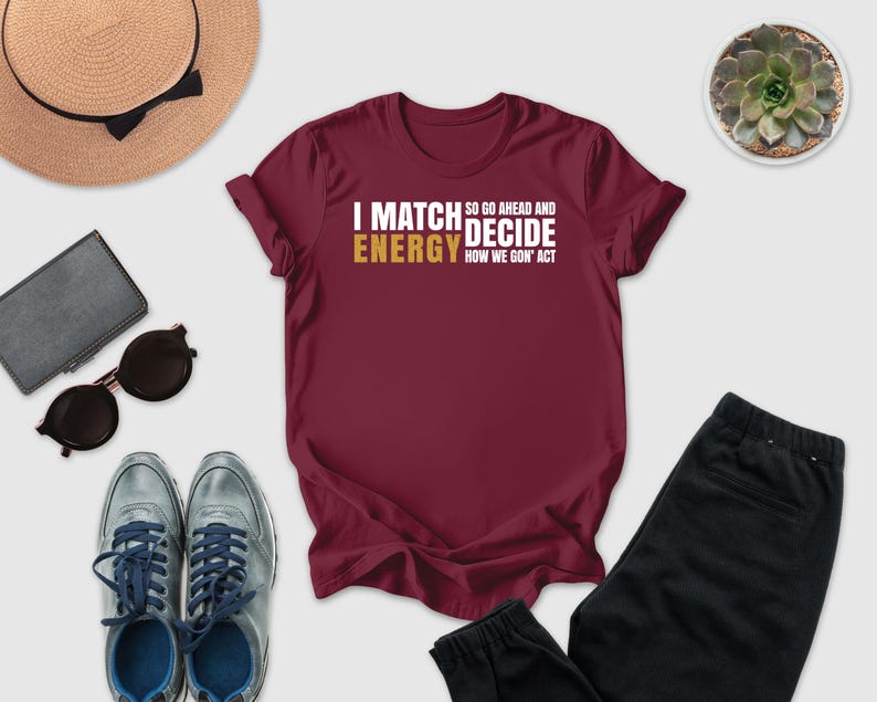 a casual outfit consisting of a burgundy t-shirt with a humorous text, a pair of gray sneakers, a hat, sunglasses, a wallet, a potted plant, and a pair of black pants.