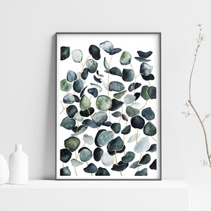 May include: A framed watercolor print featuring a cluster of eucalyptus leaves in shades of green and blue. The leaves are arranged in a vertical pattern, with some overlapping. The background is white.