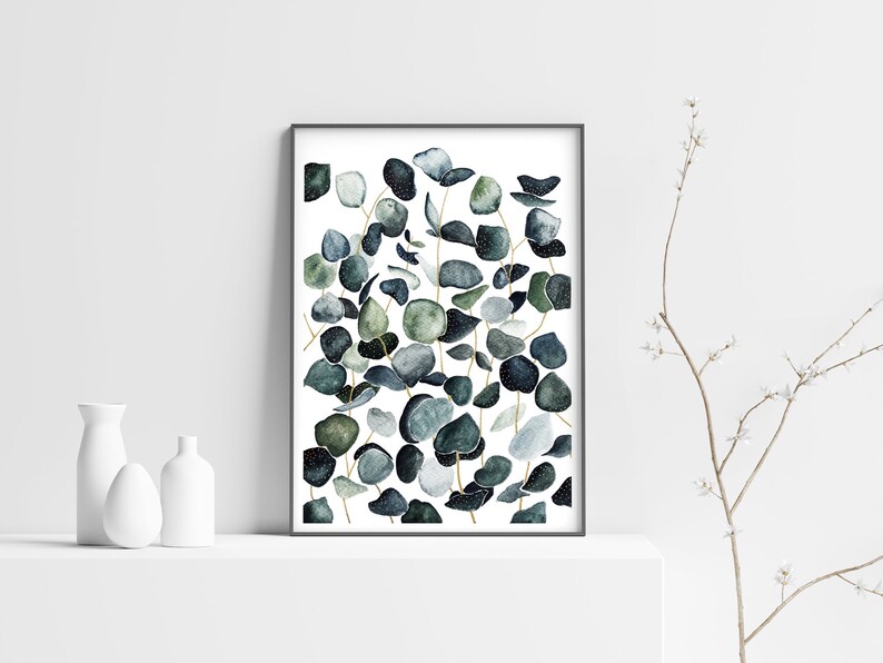 May include: A framed watercolor print featuring a cluster of eucalyptus leaves in shades of green and blue. The leaves are arranged in a vertical pattern, with some overlapping. The background is white.