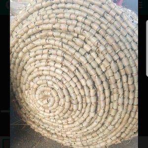 May include: Close-up of a woven mat made of natural fibers, rolled up in a spiral shape. The mat is light brown in color and has a rough texture.