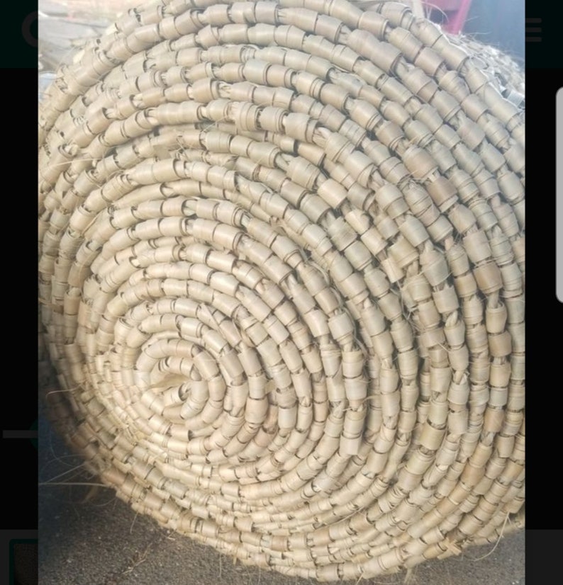May include: Close-up of a woven mat made of natural fibers, rolled up in a spiral shape. The mat is light brown in color and has a rough texture.