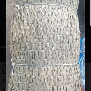 May include: A roll of natural woven material, possibly for crafting or gardening. The material is light brown and has a woven pattern. It is tied with white string.