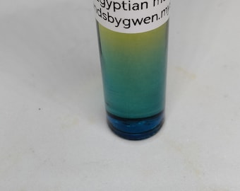 Könnte beinhalten: Eine kleine Glasflasche mit einem goldenen Verschluss und einem weißen Etikett mit der Aufschrift "Egyptian musk" und "ndsbygwen.my". Die Flasche ist mit einer gelben und blauen Flüssigkeit gefüllt.