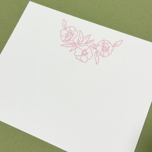 May include: A blank white card with a pink floral design in the upper right corner. The design features three stylized flowers with leaves.