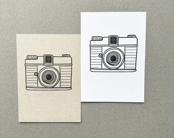 Pode incluir: Dois cartões, um com fundo marrom e o outro com fundo branco, ambos com um desenho em preto e branco de uma câmera vintage.