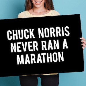 May include: A person holding a black sign with white text that reads "Chuck Norris never ran a marathon".