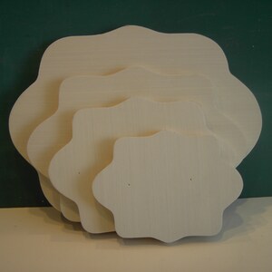 May include: Four white wooden decorative plates with scalloped edges, stacked in decreasing size. The plates are unfinished and have a smooth surface.