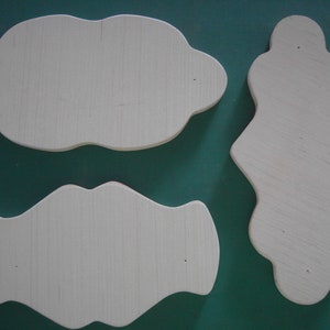 Pode incluir: Três formas de madeira branca com uma superfície lisa e ligeiramente texturizada. As formas são irregulares e têm uma aparência de nuvem. Todas são da mesma cor e têm uma textura semelhante.