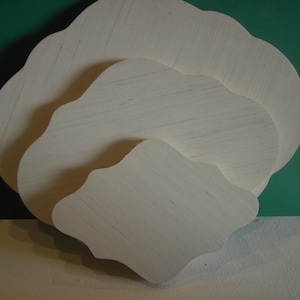 May include: Three white wooden signs with scalloped edges, arranged in decreasing size. The signs are blank and ready for painting or decorating.