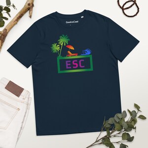 以下が含まれることがあります： 紺色のTシャツに、虹色のグラフィックがプリントされています。ヤシの木、パラソル、ビーチチェア、波のビーチシーンが描かれています。緑色の枠の中に「ESC」という文字があります。