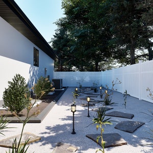 May include: A white picket fence borders a gravel pathway lined with small trees and shrubs. The pathway leads to a white house with a brown wooden door. The yard is decorated with small, flat stones and solar lights.