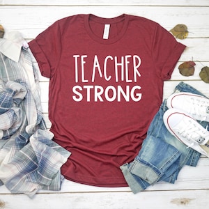 Może przedstawiać: Bordowy t-shirt z napisem "TEACHER STRONG" w białych literach.