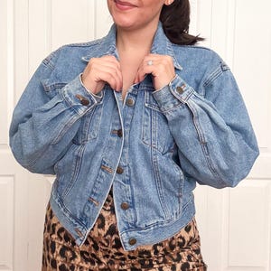 Puede incluir: Chaqueta vaquera azul claro con botones y cuello. La chaqueta tiene mangas largas con puños abotonados. La modelo lleva un pantalón con estampado de leopardo.