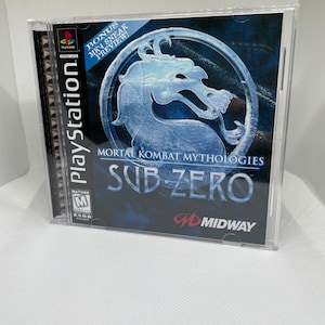 Puede incluir: Caja de juego de PlayStation para Mortal Kombat Mythologies: Sub-Zero. La portada presenta un diseño de dragón azul y el título del juego. La caja incluye el logotipo de PlayStation y la clasificación ESRB.
