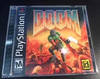 May include: A PlayStation game case for the video game "DOOM." The cover art features a green-armored character firing a weapon, set against a fiery, hellish landscape. The game's title is in large, bold orange letters.