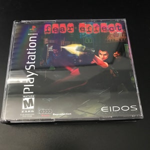 May include: A PlayStation game case for the game "Fear Effect" with a mature rating. The case is black with a red and white label. The label features a woman holding a gun in a dark alley. The text "Eidos Interactive" is on the bottom right corner of the label.