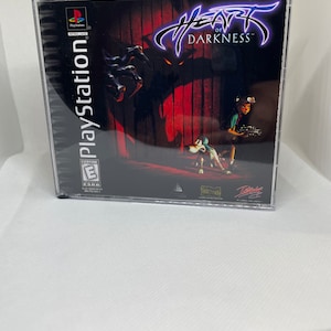 May include: PlayStation game case for Heart of Darkness. The case is black with a red and black background image. The title "Heart of Darkness" is in white with a purple outline. The PEGI rating is "3" and the game is published by Fox Interactive.