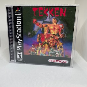 Puede incluir: Una caja de juego de PlayStation para Tekken, un juego de lucha. La caja es negra con un logotipo rojo y blanco. El juego está clasificado como T para adolescentes por la ESRB. La parte posterior de la caja presenta un grupo de personajes del juego, incluidos Heihachi Mishima, Kazuya Mishima y Paul Phoenix. La caja está hecha por Namco.