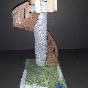 May include: A miniature stone tower with a wooden spiral staircase and a small blue pond at the base. The tower has a stone wall and a wooden railing at the top.