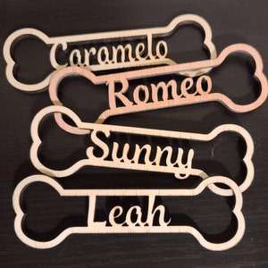 May include: Four wooden dog bone-shaped tags with the names "Caramelo", "Romeo", "Sunny", and "Leah" engraved on them.