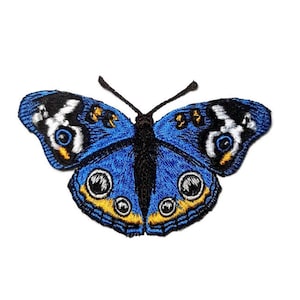 Puede incluir: Parche bordado de mariposa azul con detalles en negro, blanco y amarillo. La mariposa tiene ojos grandes y redondos.