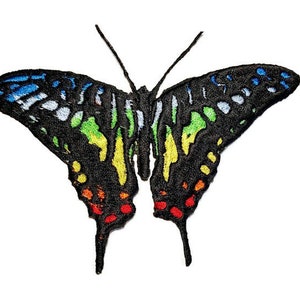 Puede incluir: Un parche bordado con una mariposa con un patrón de degradado arcoíris. La mariposa tiene contornos negros y un cuerpo negro.