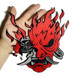 May include: Embroidered patch featuring a red and black Oni mask with flames, a silver robotic eye, and a silver chain.