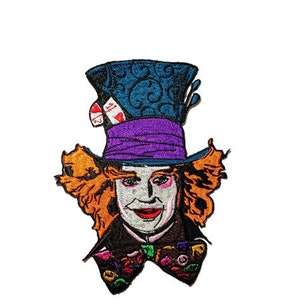 May include: Embroidered patch featuring the Mad Hatter from Alice in Wonderland. The patch depicts the character's face, wearing a tall blue hat with a purple band, orange hair, and a colorful bow tie. The design is set against a white background.