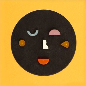 May include: A black circle with various colored shapes on it, including a blue crescent, a pink half-circle, a yellow circle, a white irregular shape, a yellow triangle, and a red half-circle.