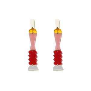 May include: A pair of colourful geometric earrings with pink, red, yellow and white accents. The earrings are made of acrylic and have a modern, abstract design.