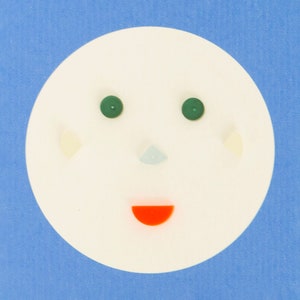 May include: A white oval with a green, blue, and red face. The face has two green eyes, a blue nose, and a red mouth.