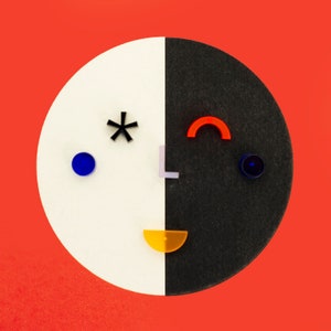 May include: A black and white circle with a red, orange, blue, and white geometric design. The design resembles a face with a star for an eye, a curved line for an eyebrow, and a half-circle for a mouth.