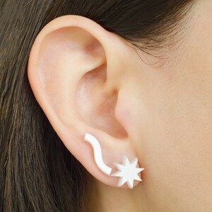 May include: A pair of white earrings, one shaped like a star and the other a curved line.