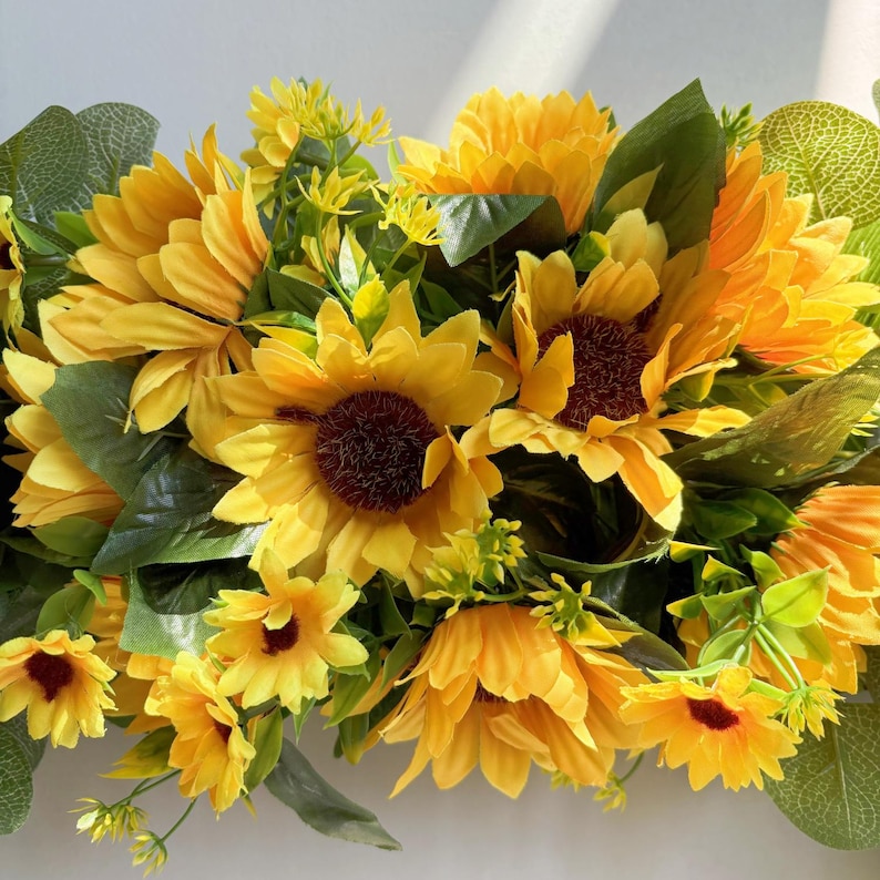 May include: A yellow sunflower garland with green leaves. The garland is made of artificial flowers and is perfect for adding a touch of summer to your home decor.